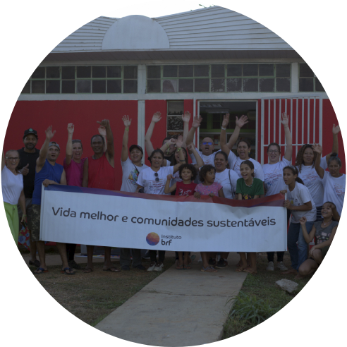 Foto de um grupo de voluntárias e voluntários do Instituto BRF e da comunidade em frente à biblioteca. Eles seguram um banner com o logo do Instituto BRF e a frase “Vida melhor e comunidades sustentáveis”. Estão sorrindo e alguns estão com os braços levantados.