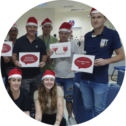 Foto de um grupo de voluntárias e voluntários do Instituto BRF com gorros natalinos e segurando placas com mensagens sobre doação de sangue.