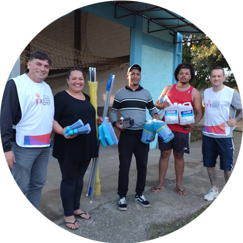 Foto de dois voluntários do Instituto BRF junto com uma mulher e dois homens com produtos de limpeza nas  mãos.