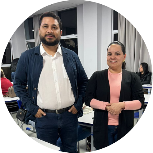 Foto de um homem e de uma mulher em pé, bem próximos um do outro, em uma sala de aula.