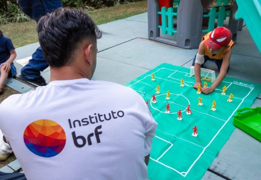 Foto de um voluntário do Instituto de costas enquanto joga futebol no chão com uma criança.