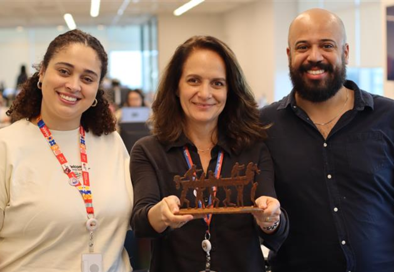 Foto de Sulamita Leitão, Raquel Ogando e Caique Eduardo Silva em pé e bem próximos. Raquel segura nas mãos o troféu Heróis da Pátria.