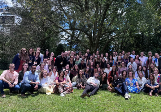 Foto da delegação brasileira em uma área externa bastante arborizada. Parte do grupo está em pé e outra parte sentada em um gramado. Todos estão sorrindo.