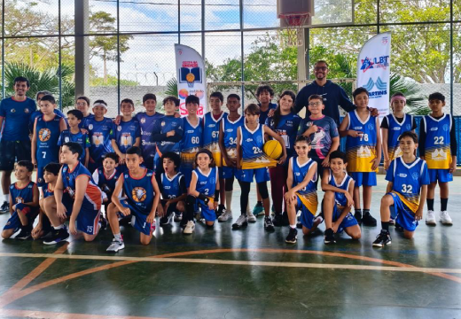 Foto posada de um grupo de crianças e dois homens em uma quadra esportiva coberta. Um dos meninos segura uma bola de basquete.