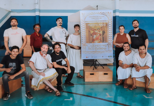 Foto posada do grupo de atores e responsáveis pelo projeto Multiplicando ao lado de um banner da peça.