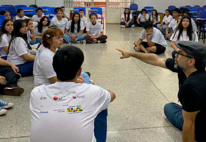 Foto de um grupo de estudantes sentados no chão junto com um instrutor e um voluntário do IMBRF.
