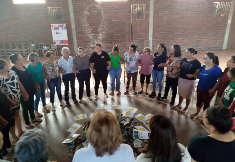 Foto de um grupo de pessoas em pé formando um círculo. No centro da roda, há papéis espalhados no chão.