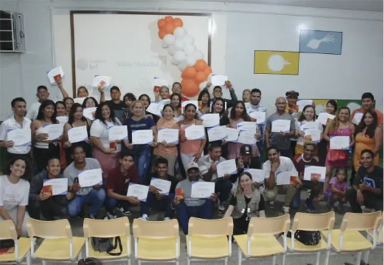Foto de um grupo diverso de pessoas, em pé e sentadas, mostrando seus certificados de conclusão do curso de língua portuguesa.