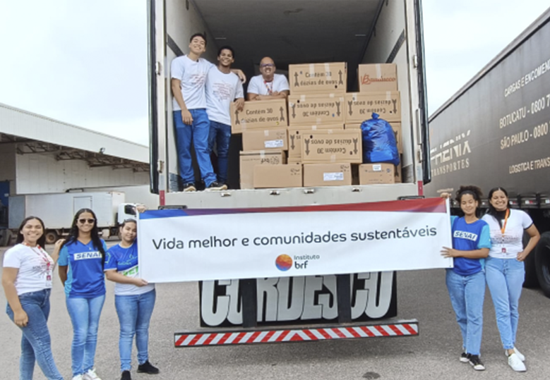 Foto de um grupo de voluntárias segurando o banner do Instituto BRF em frente a um caminhão com a porta aberta. Dentro dele, há um grupo de voluntários ao lado de várias caixas com doações para o Rio Grande do Sul.