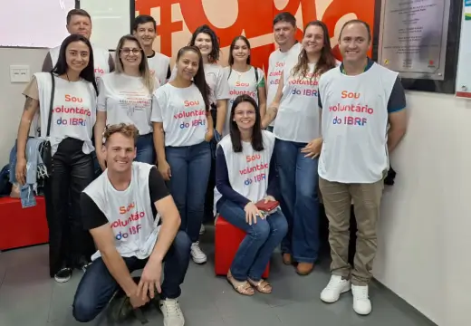 Foto de um grupo de voluntários e voluntárias, em pé e sentados, em uma sala do hemocentro. Todos usam coletes do programa de voluntários da BRF e sorriem.