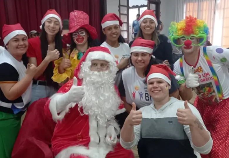 Foto de um grupo de voluntárias e voluntários do Instituto BRF ao redor de uma pessoa vestida de Papai Noel em um ambiente interno.