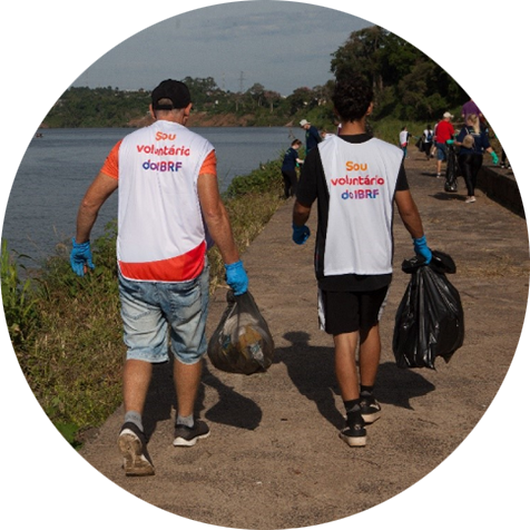 Foto de dois voluntários do Instituto BRF levando sacos de plástico com os resíduos recolhidos.