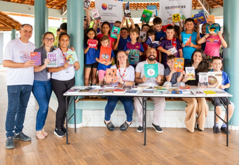Foto de um grupo de pessoas voluntárias com crianças em uma escola. Todos seguram livros e sorriem.