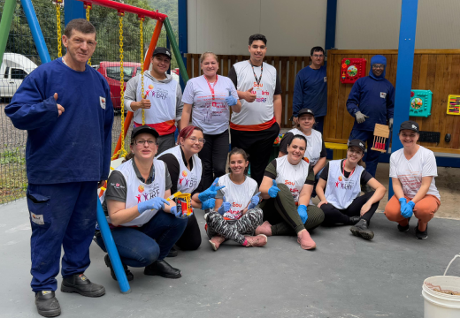Foto de parte das pessoas voluntárias participantes na ação de montagem do jardim sensorial. Elas estão próximas ao balanço, em pé e algumas sentadas. Todas sorriem.