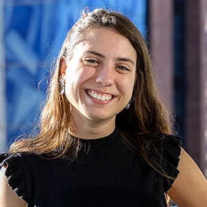 Foto de Laura Simões Camargo, uma mulher branca, com cabelos lisos compridos. Ela usa uma blusa preta e sorri.