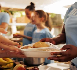 Foto das mãos de uma pessoa entregando embalagem de isopor com comida para outra pessoa.