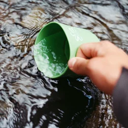 Foto da mão de uma pessoa pegando água com uma caneca.
